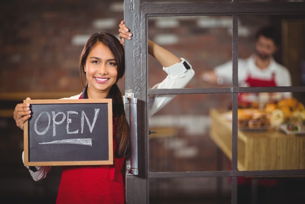 smiling business owner showing chalkboard with open sign